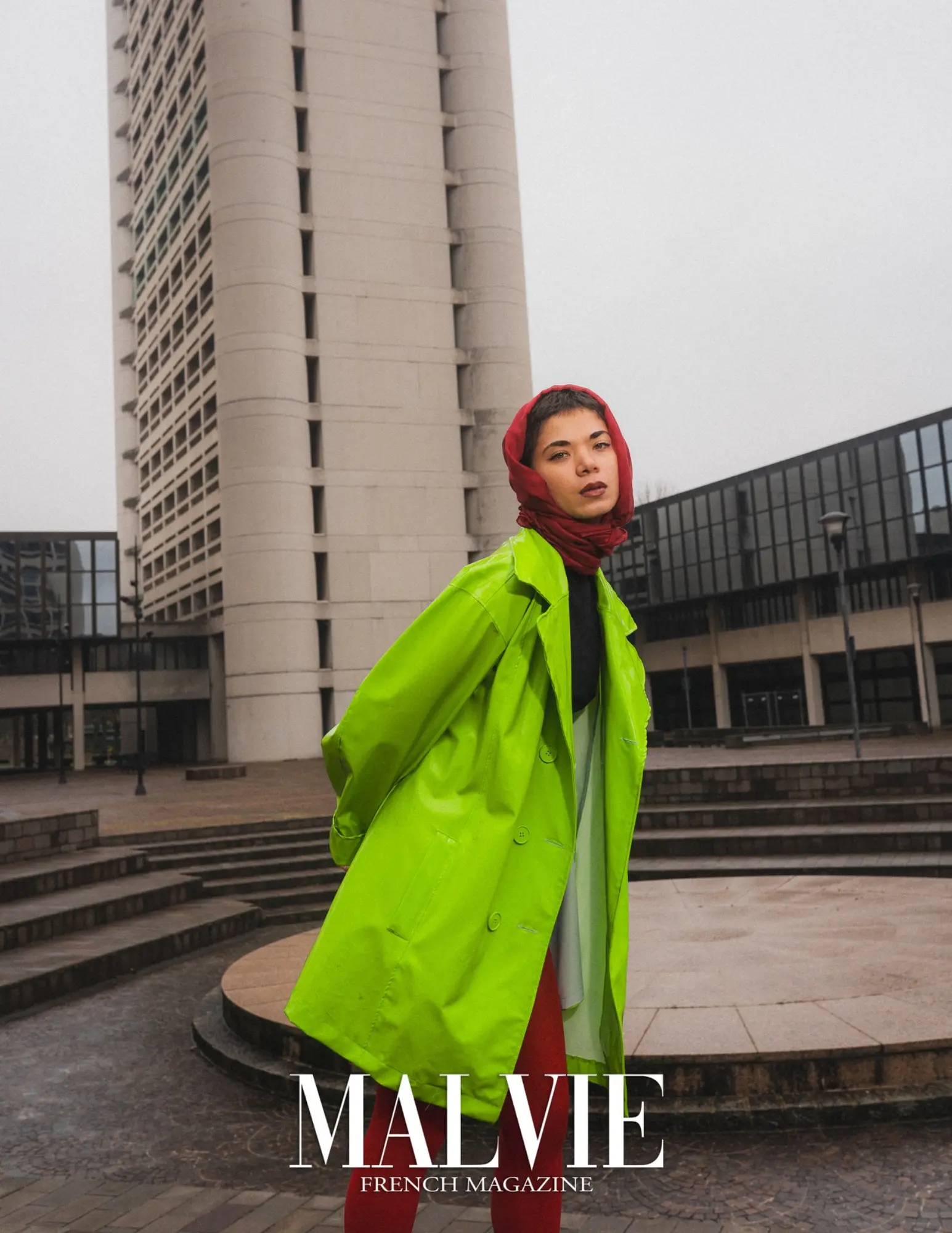 A fashion portrait combines a still pose, red garment and a stark architectural setting.
