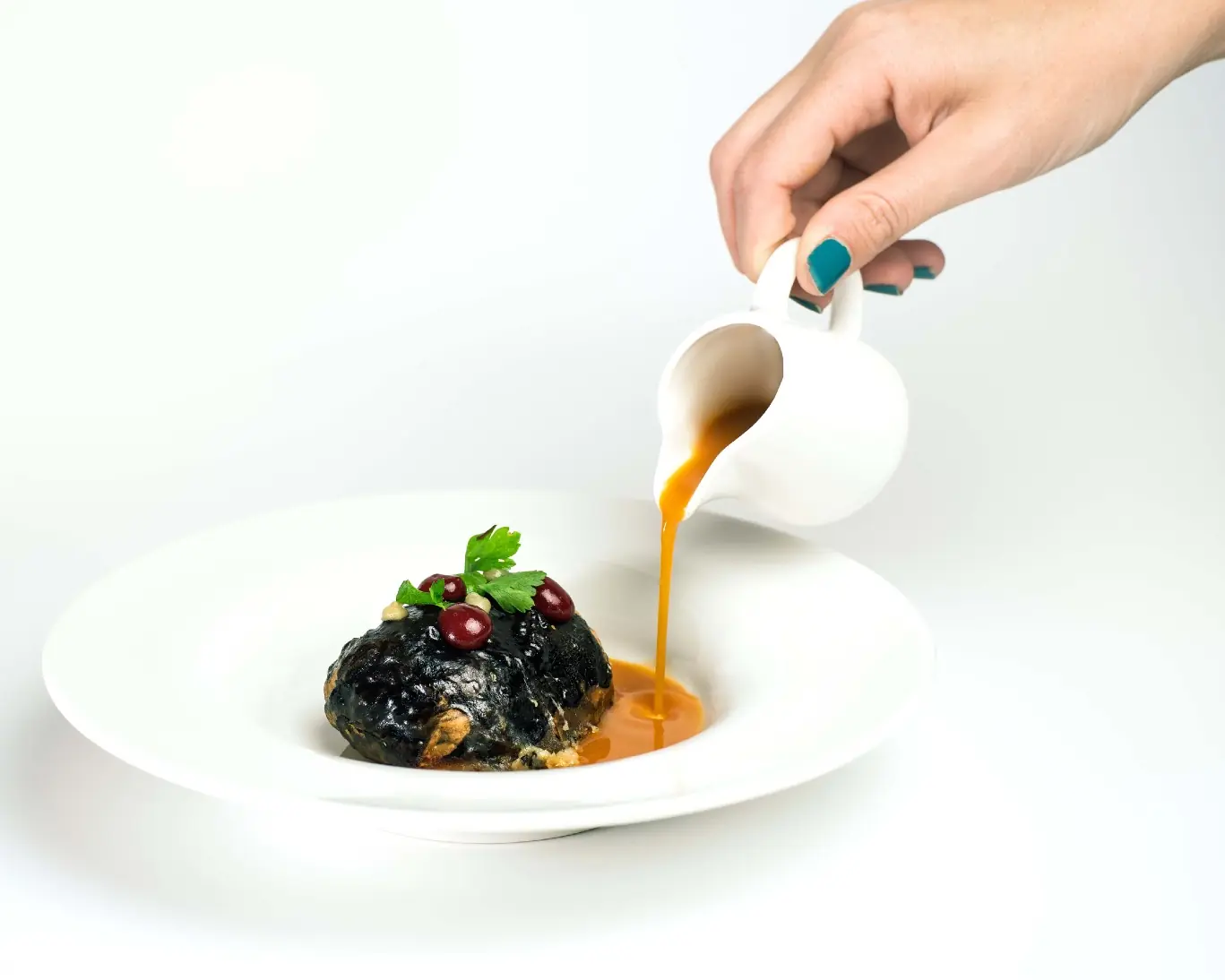A dark sauce is poured over a plated dish on a restaurant table.