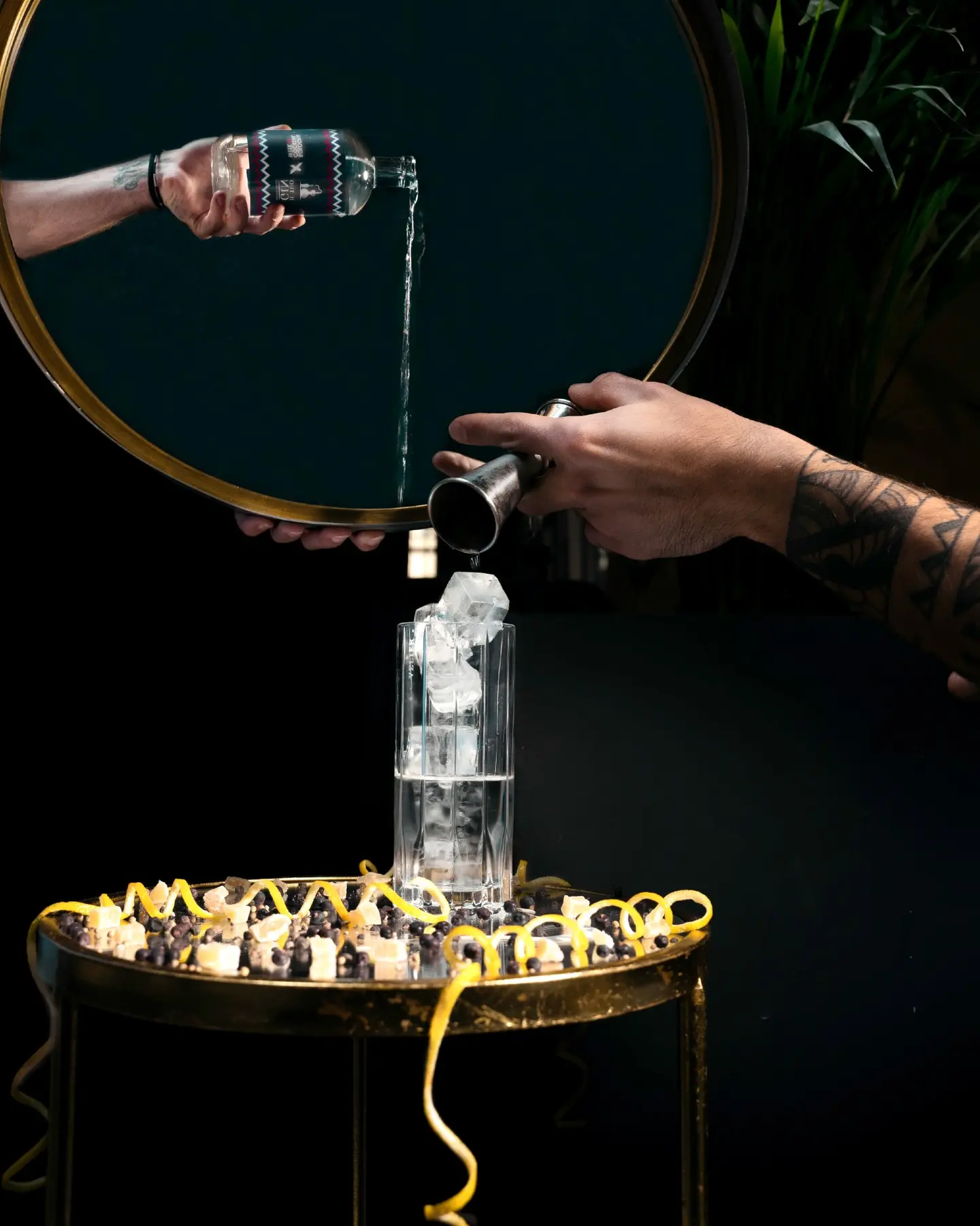 A bartender pours a pale cocktail into a stemmed glass in a dark interior.