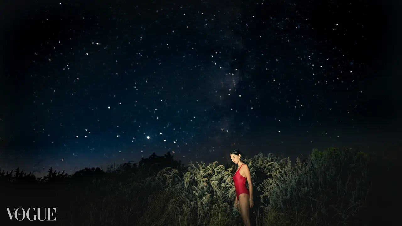 A distant figure in red stands below a star-filled night sky, surrounded by a dark field.