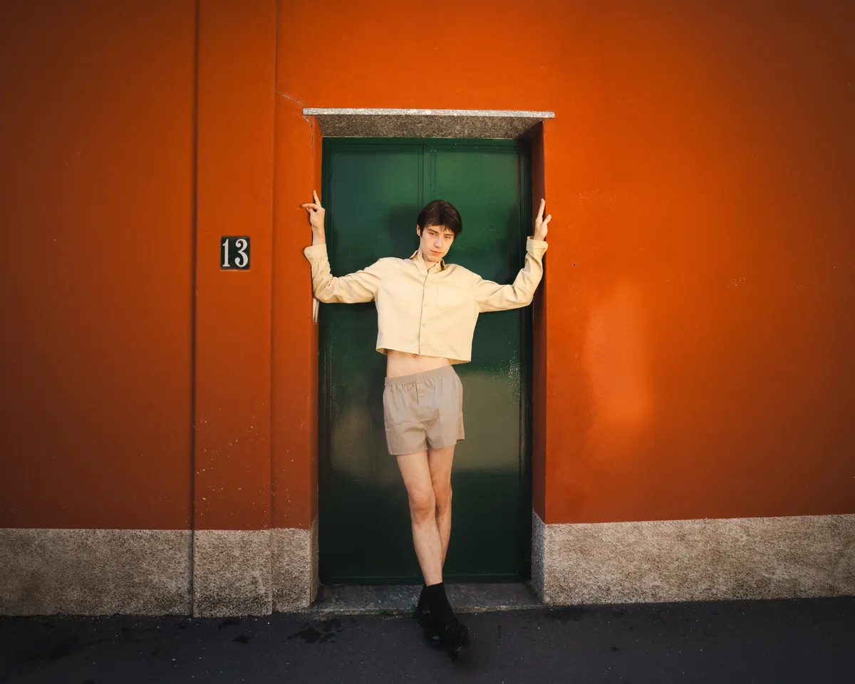 A figure in dark clothing stands at a red doorway in a white wall.