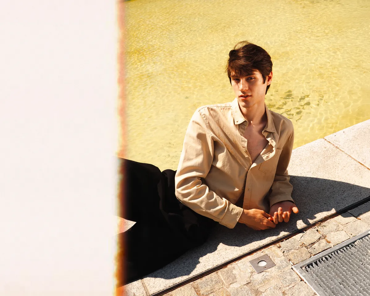 A figure crosses a mustard-yellow wall with a red garment and long cast shadow.