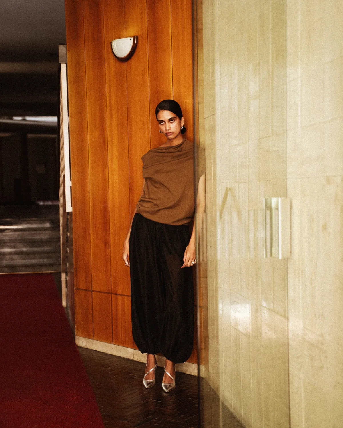 A model occupies a timber-lined interior with an angular, folded pose.