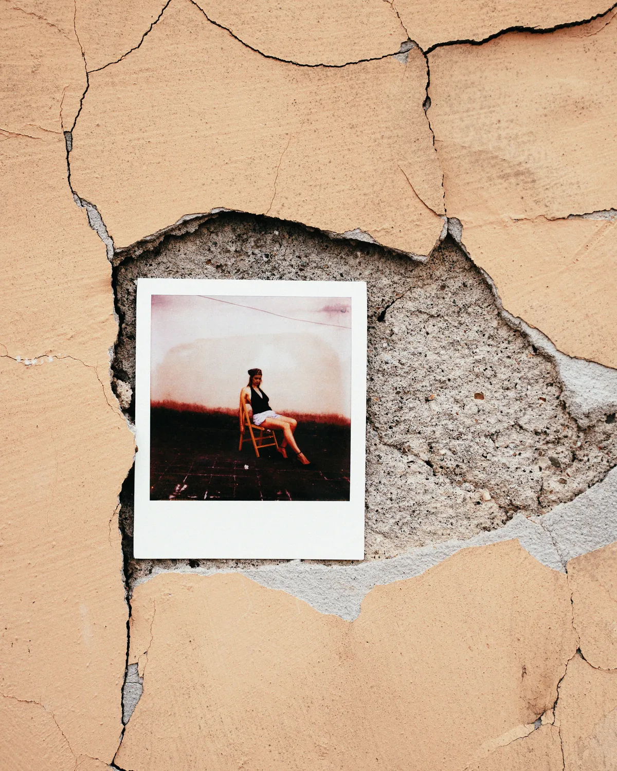 A hand-held instant photograph interrupts a textured urban wall.