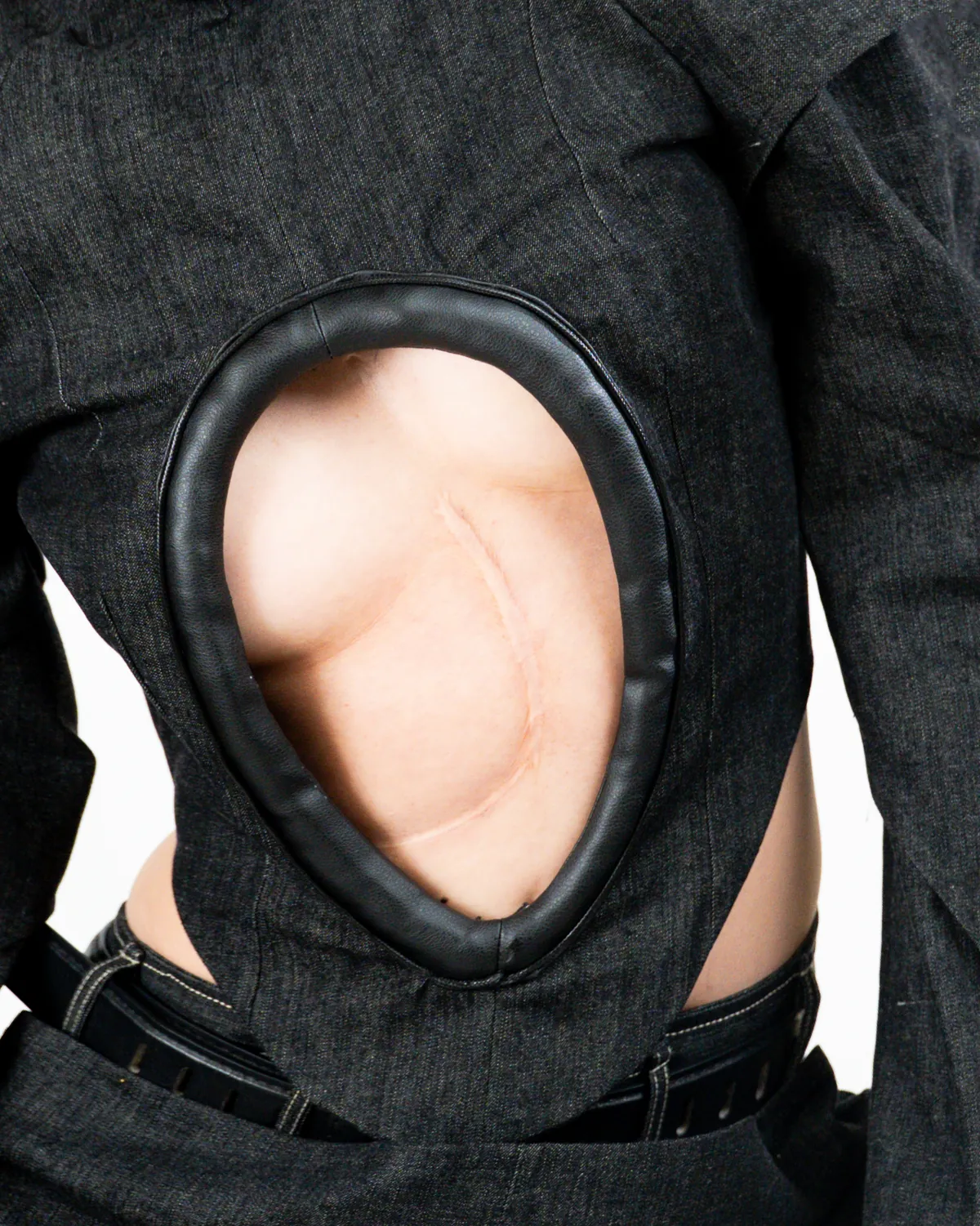 A circular cut-out in a black garment frames the skin of a bent torso.