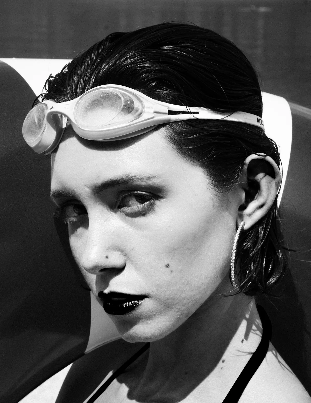 A face wearing swim goggles breaks the surface of green-blue water.